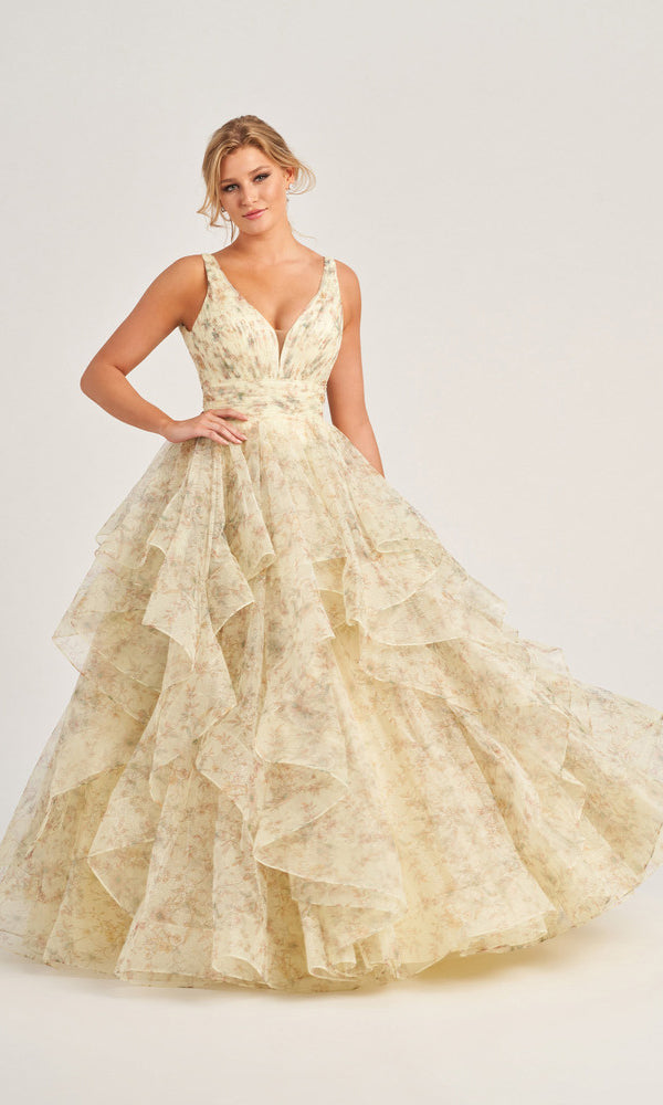 A woman stands against a light background wearing the Colette Tiered Long Print Prom Ball Gown CL5273, featuring a sleeveless V-neck, floral print, and layered ruffled tulle skirt.